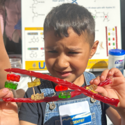 A young boy holding two pieces of licorice crossed, with gummy bears on toothpicks holding the strands together 