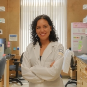 Olga Jaime in a white lab coat, standing in a lab.