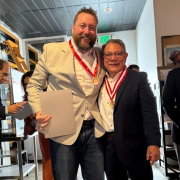 John Billimek and Cesar Aranguri stand together with medals around their necks. Aponte and Casafrancas are in the background.
