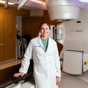 Megan Daly, MD, stands in front of a radiotherapy system within a hospital room