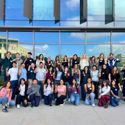 2026 Income PhD student orientation group photo of approximately 40 people posing in front of a modern glass building, many making UCI Zot hand signs.
