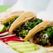 Three tacos with lime and radish garnish on the side
