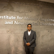 Vivek Swarup, Ph.D., standing against the Institute for Memory Impairments and Neurological Disorders wall