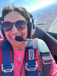 Curlin, with a headset on, in the airplane. You can see the skyline behind her, out of the plane window.