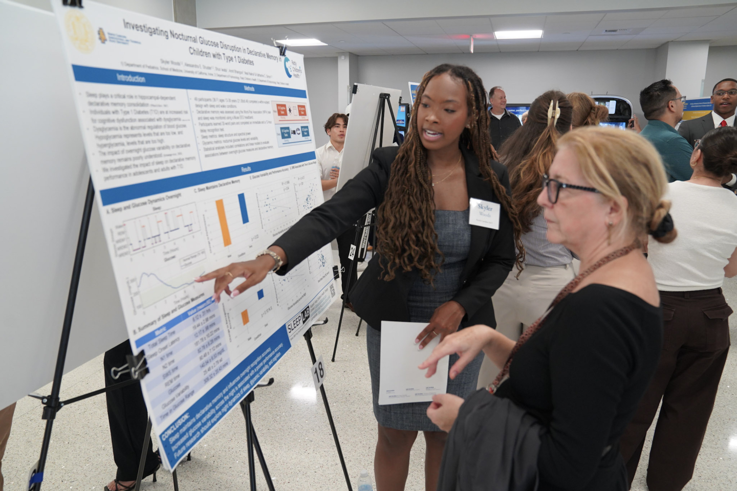 A student is pointing at a poster, talking with an attendee.