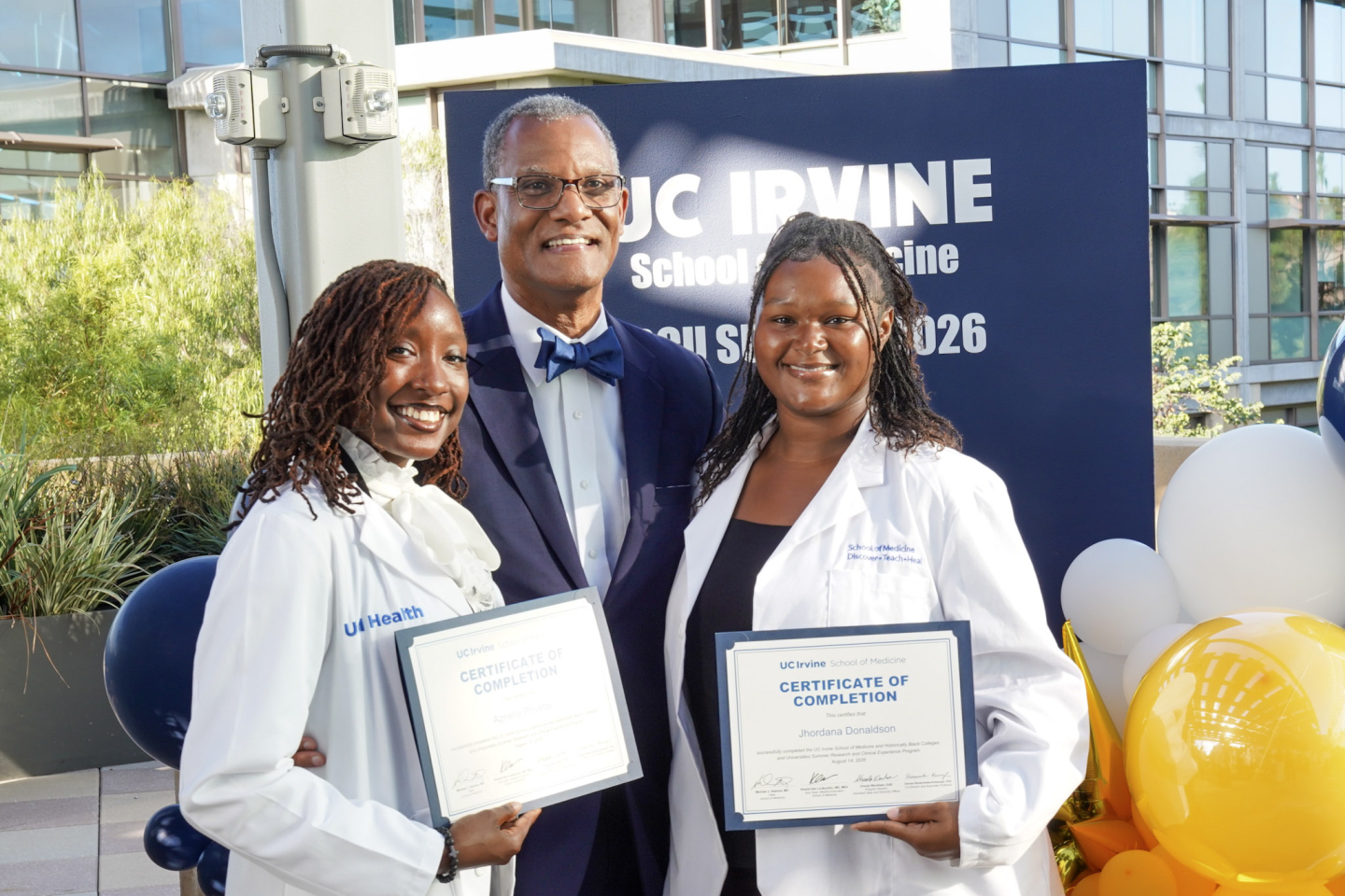 Dr. Seard stands with two students at his side, each holding a certificate of completion. 