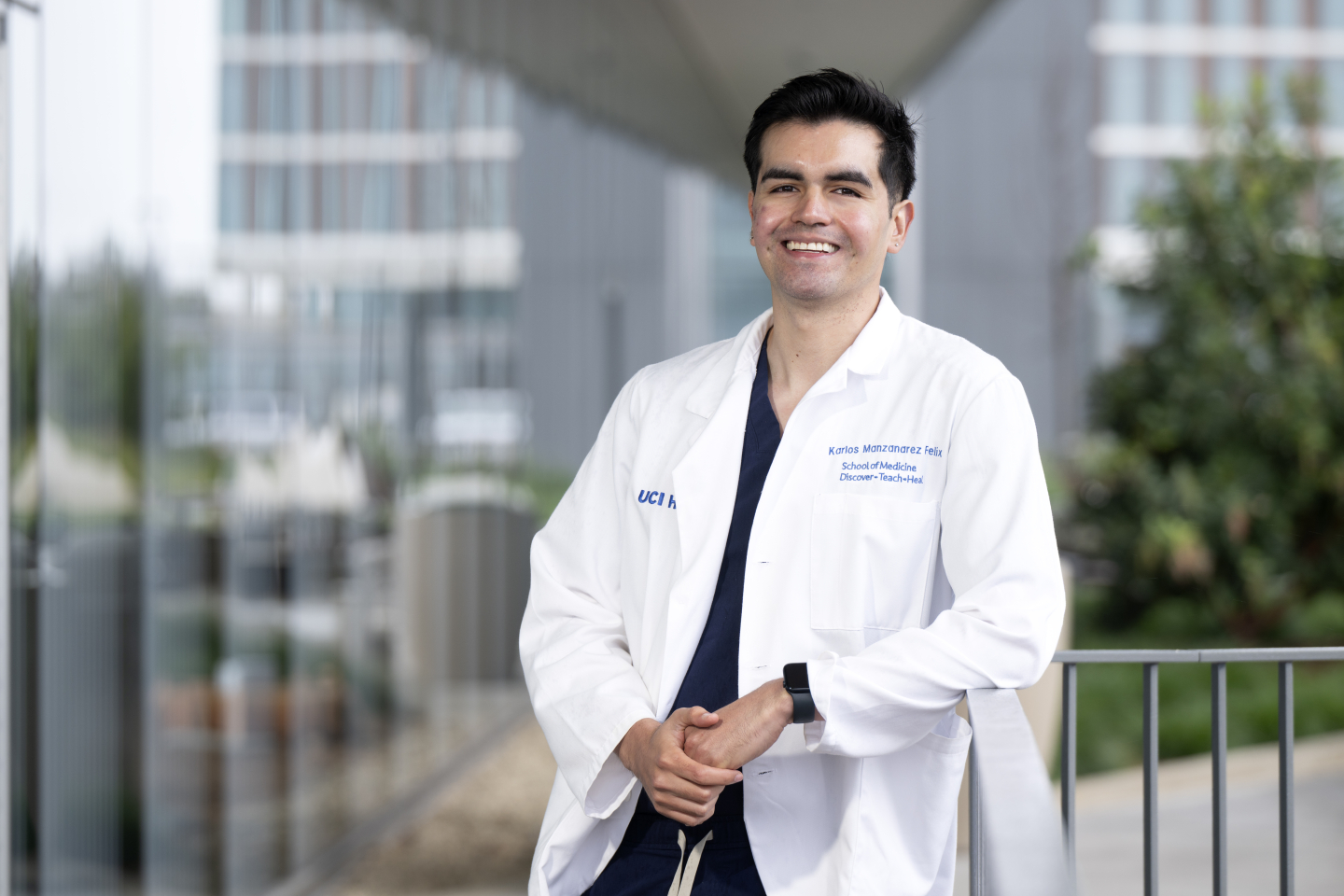 Karlos Manzanarez stands in his white coat at UC Health - Irvine. The hospital is in the backdrop.