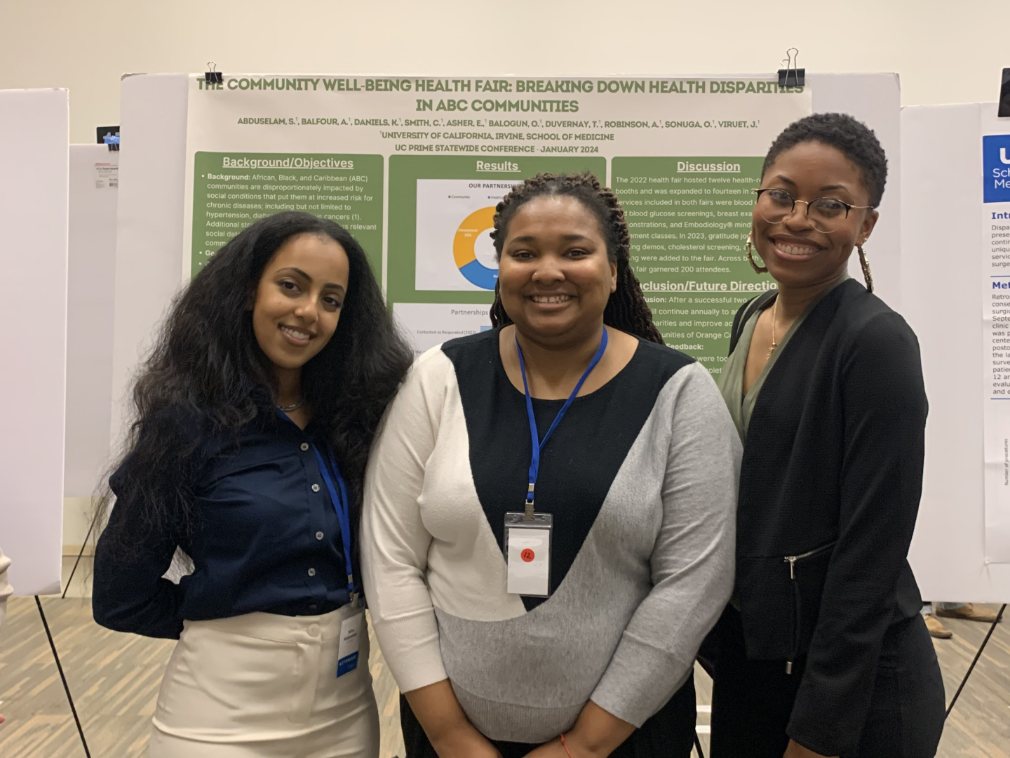 The three women stand in front of a poster titled, “The Community Well-Being Health Fair: Breaking Down Health Disparities in ABC Communities.”
