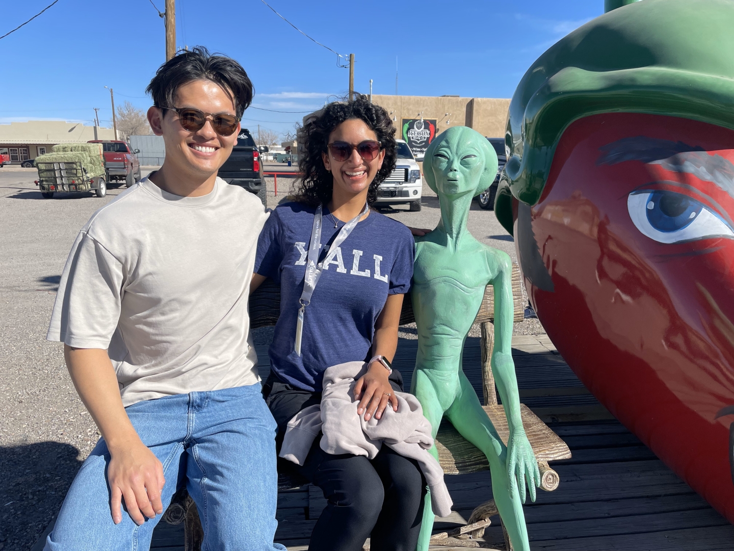 Yang and Curlin sit on a bench, next to a green statue of an alien and an oversized statute of a red chili pepper.