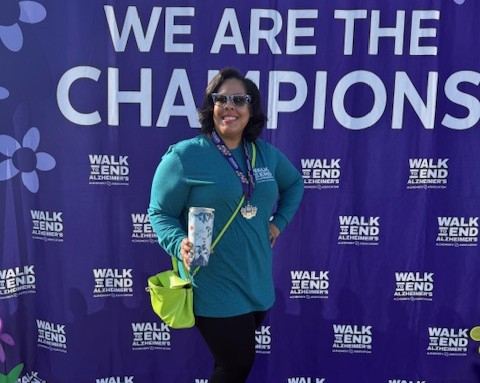 Glover stands in front of a step-and-repeat banner that says "We are the Champions" and "Walk to End Alzheimer's"
