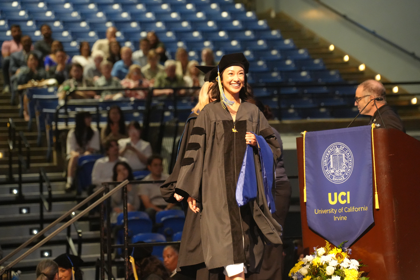 Emily Tom walking toward the podium on stage for the hooding