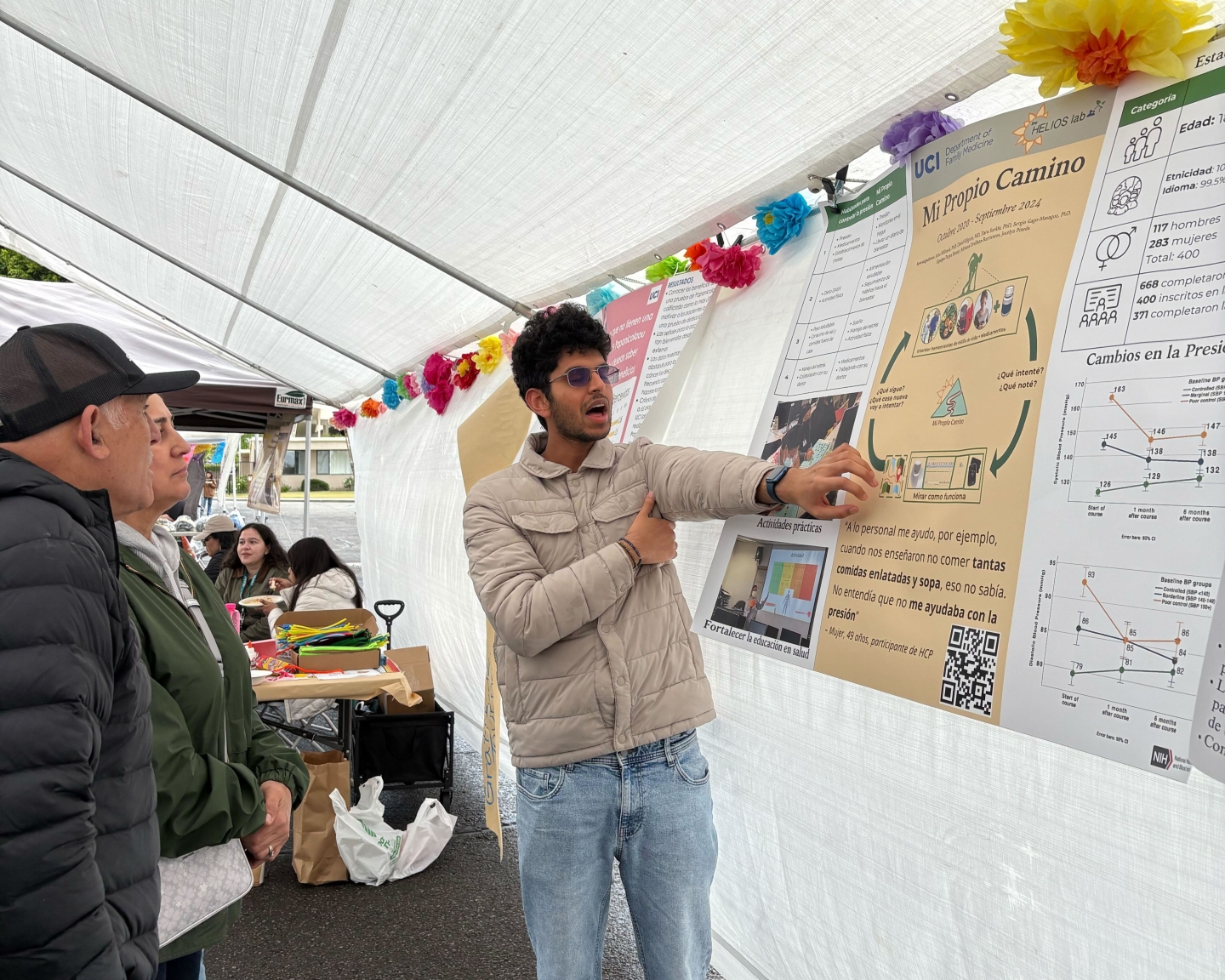 A student stands pointing at a poster while talking with a man and a women.