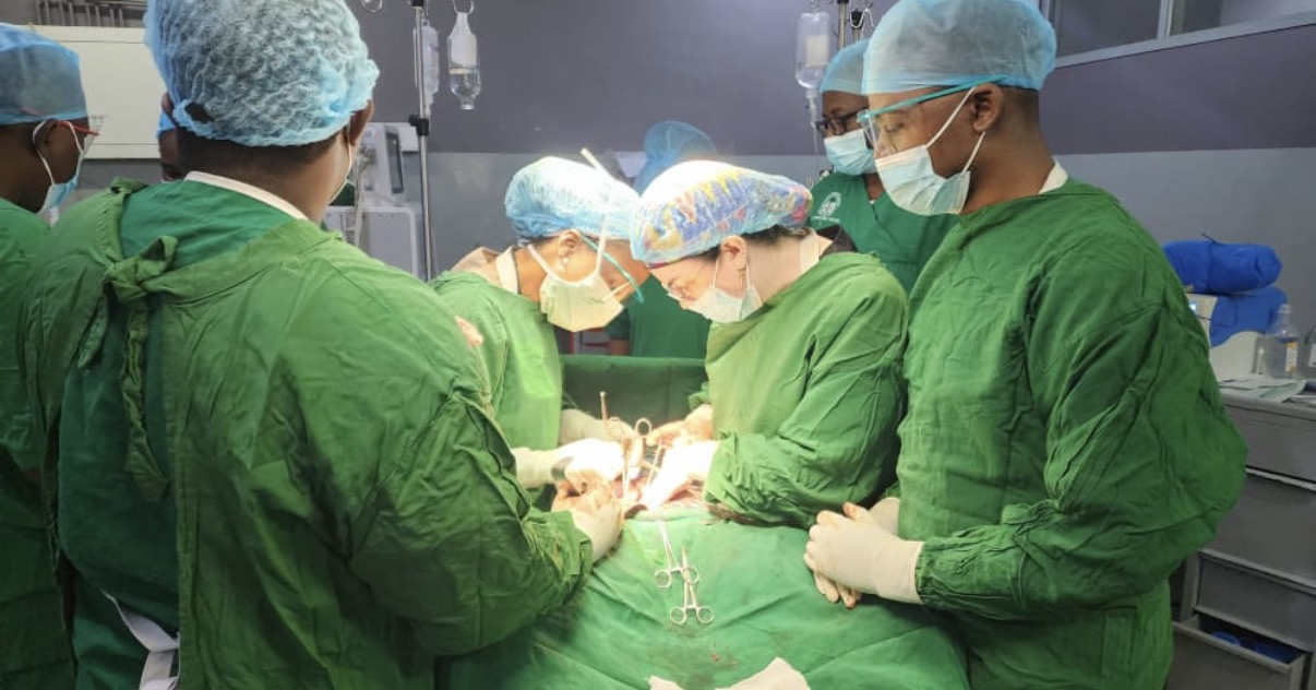 Two people operating on a patient, with several others standing near the patient as well