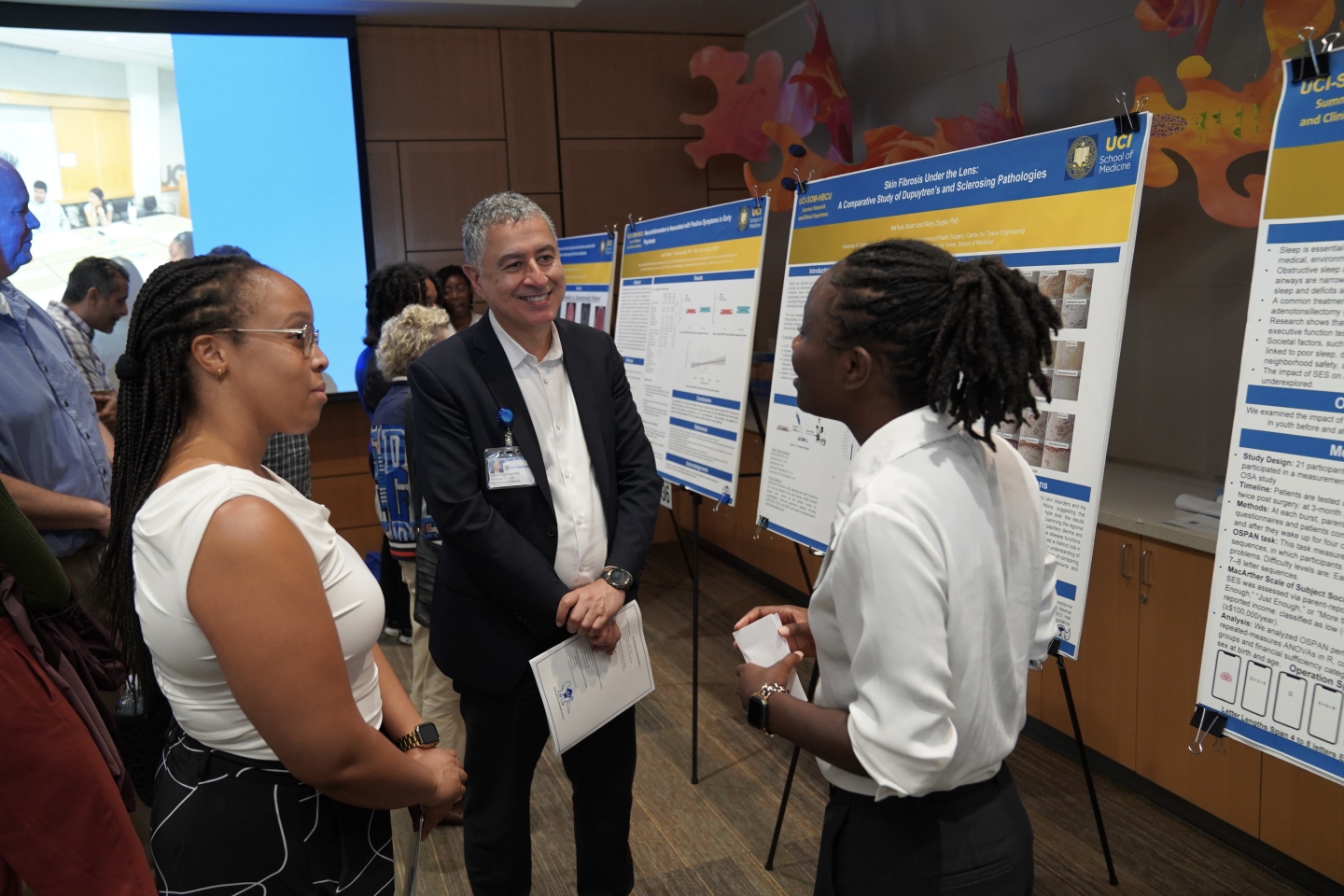 A student stands in front of a poster, talking with two other people.