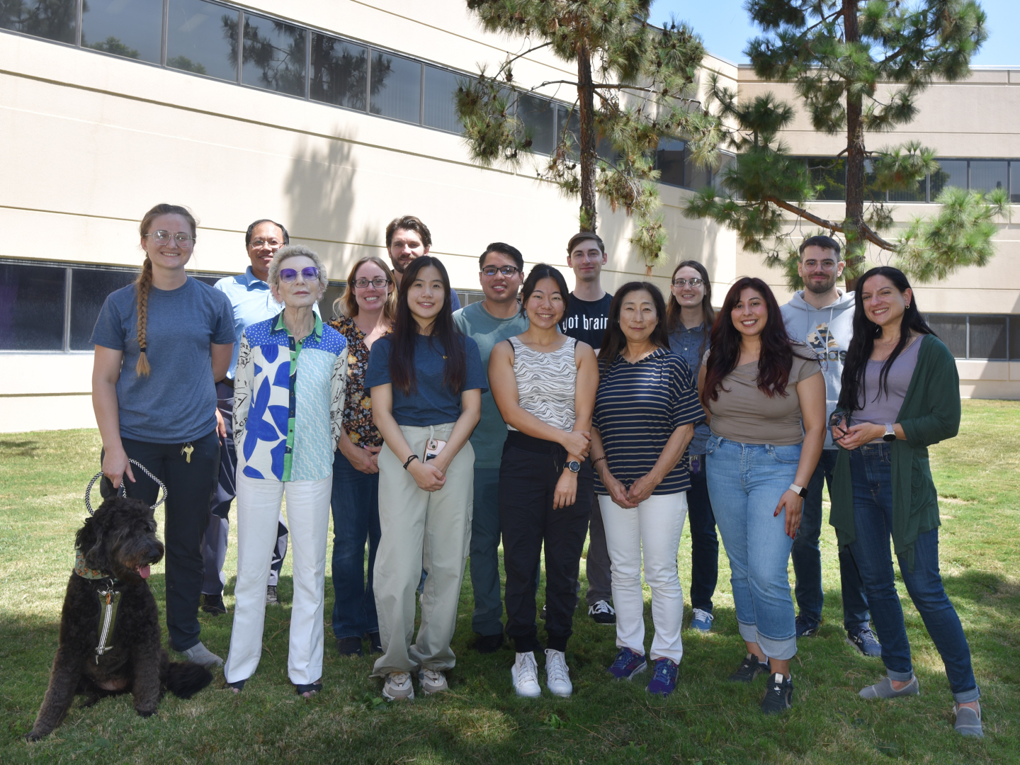 A group photo of 14 people and one dog, standing outside at UC Irvine.