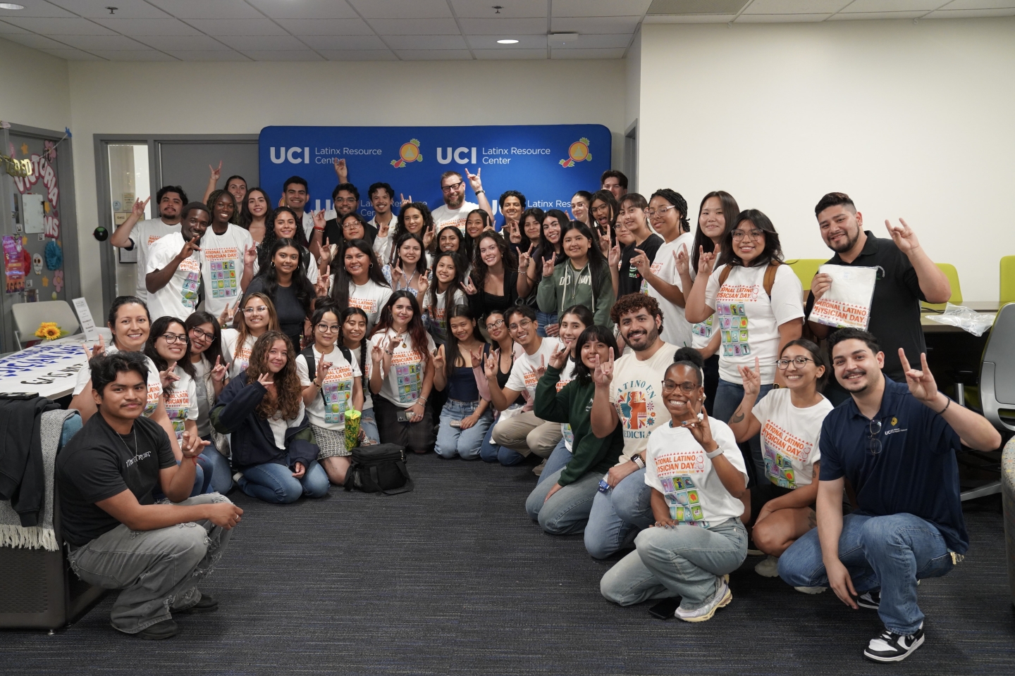 A large group of people gather together, doing the UC Irvine "zot" sign.