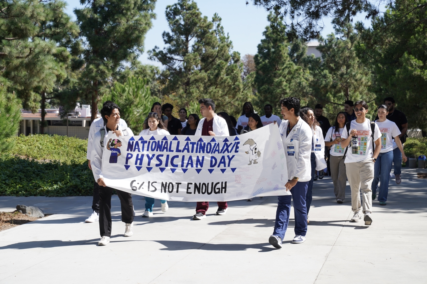 Alen and Christian hold a banner that reads National Latino/a/x/e Physician Day: 6% is not enough.