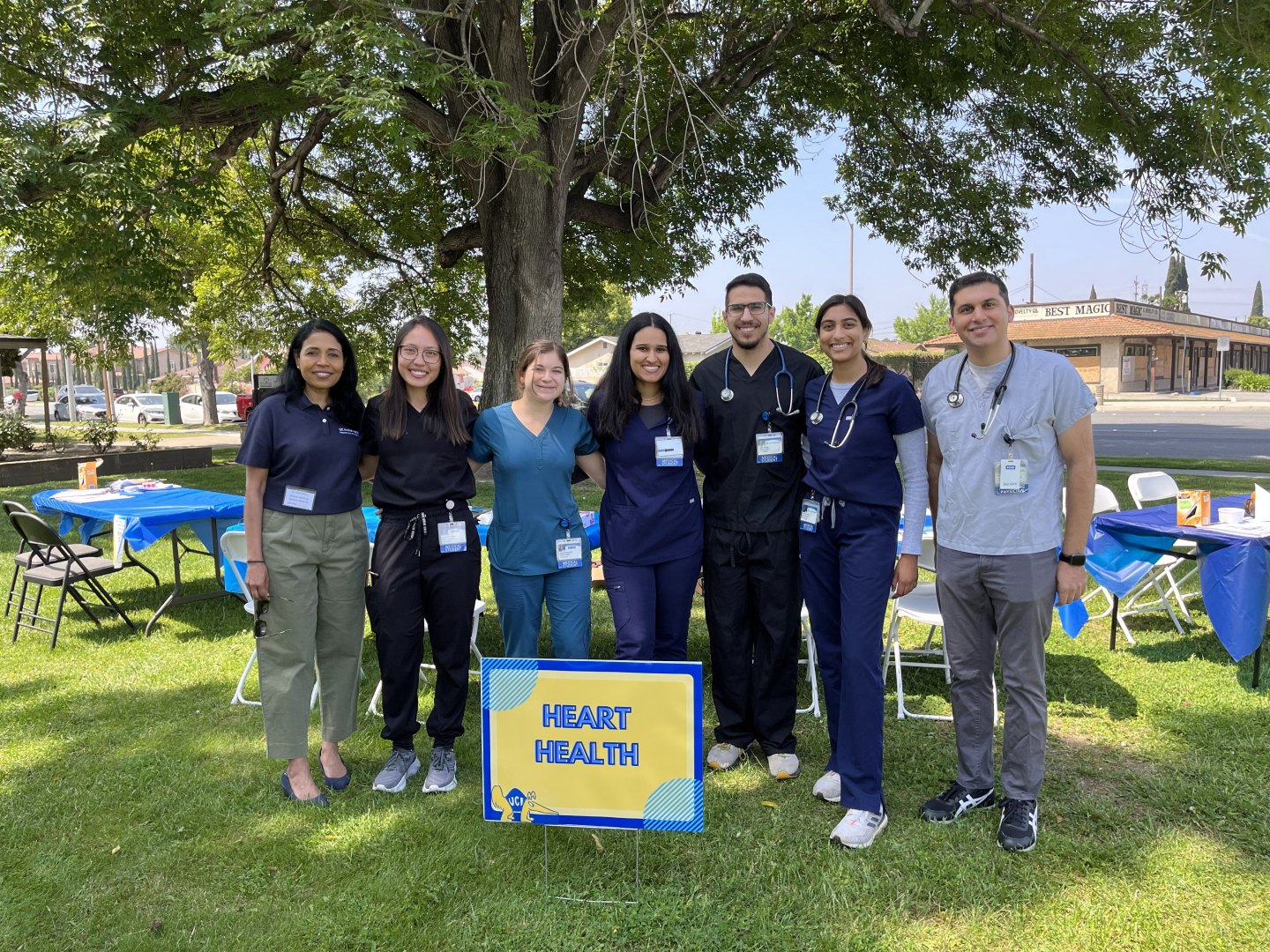 Seven people standing in a park, most in scrubs and a few with a stethoscope around their neck. In front of them is a sign that reads “Heart Health.”