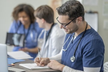 Group of healthcare students wearing scrubs attending class together, seated in a classroom doing course work.