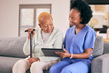 Nursing home patient and nurse sit down on couch and look at an ipad screen together